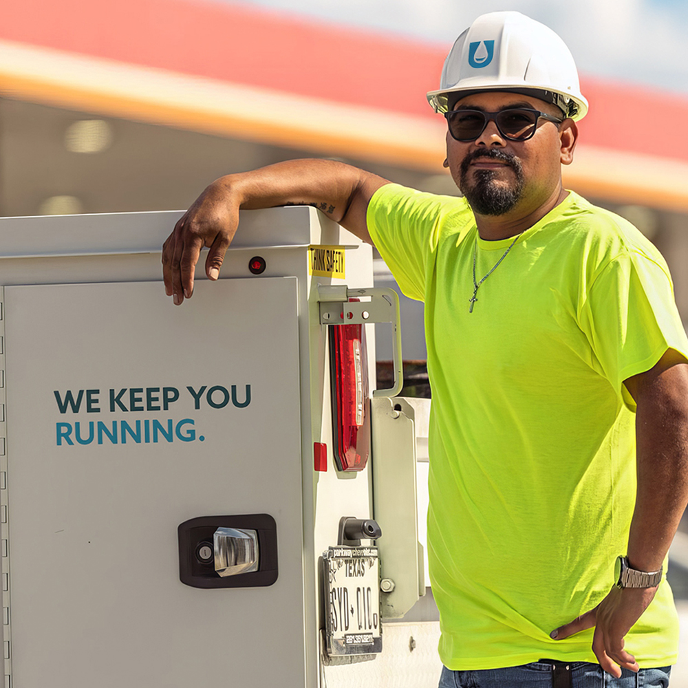 Service technician beside an open equipment cabinet at a fueling site