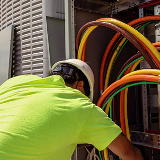 Technician working inside an open electrical enclosure with heavy feeder conductors