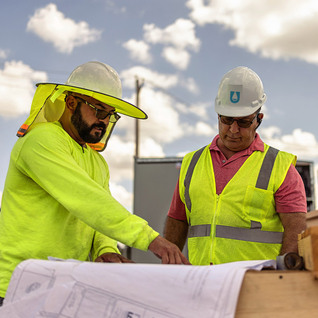 Two crew members in hard hats reviewing electrical site drawings for an EV charger project
